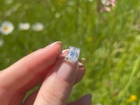 A beautiful continuum silver two carat emerald shape moissanite ring, displaying the rainbow fire that is unique to this unique gemstone. This video has been shot in a field with wild flowers and you can hear the birds and wildlife in the back ground.