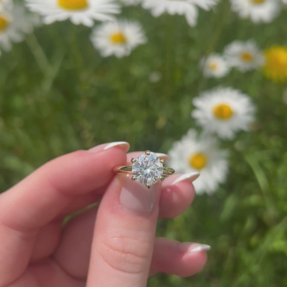 A beautiful gold and two carat moissanite ring, displaying the rainbow fire that is unique to this unique gemstone. This video has been shot in a field with wild flowers and you can hear the birds and wildlife in the back ground.