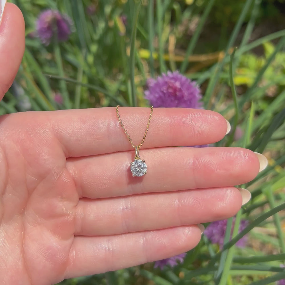 A beautiful gold and one carat moissanite pendant, displaying the rainbow fire that is unique to this unique gemstone. This video has been shot in a field with wild flowers and you can hear the birds and wildlife in the back ground.