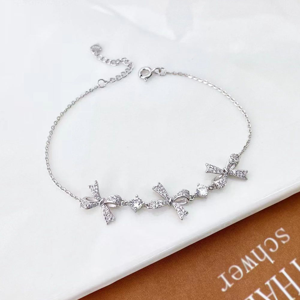 Embrace elegance with this charming sterling silver bracelet. Designed with a delicate chain and adorned with beautiful bow-shaped accents, each encrusted with sparkling cubic zirconia, this piece is perfect for adding a touch of sophistication to any outfit. The intricate bows and dazzling stones create a playful yet refined look. Additionally, the sterling silver is rhodium plated to prevent tarnishing and ensure long-lasting shine.